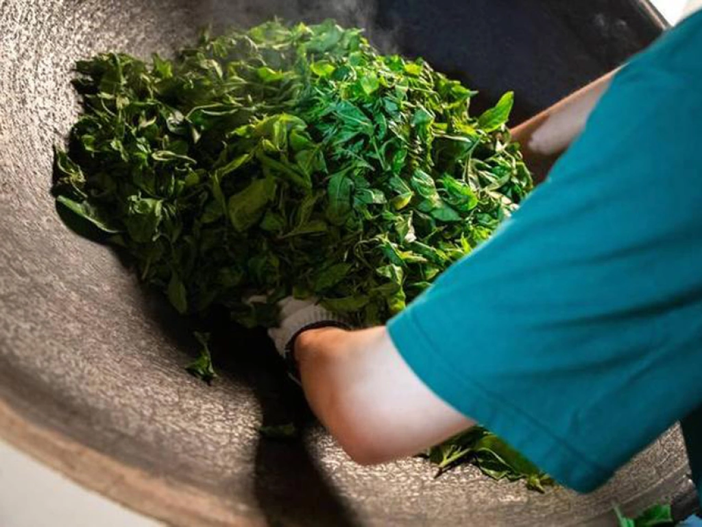 Focus on a tea master stirring tea leaves by hand in an iron pot