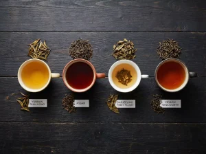 a dark wooden table showing four cups of black tea side by side: bright golden Yunnan Dian Hong, bold dark red Assam