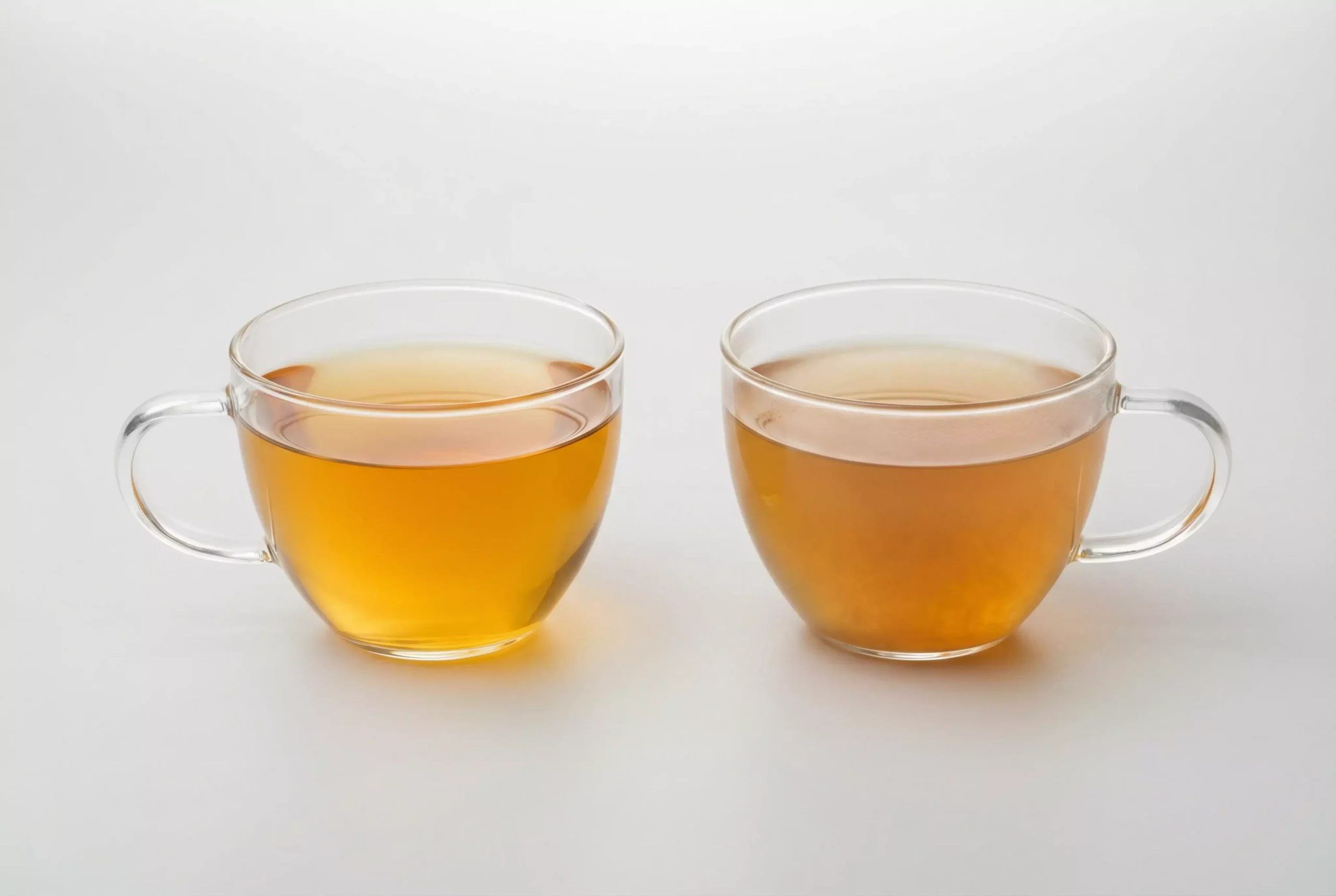 A side-by-side comparison. On the left, a transparent glass teacup filled with clear, amber raw Puerh tea liquor, showing vibrant clarity. On the right, a similar cup with visibly cloudy, darker liquor.