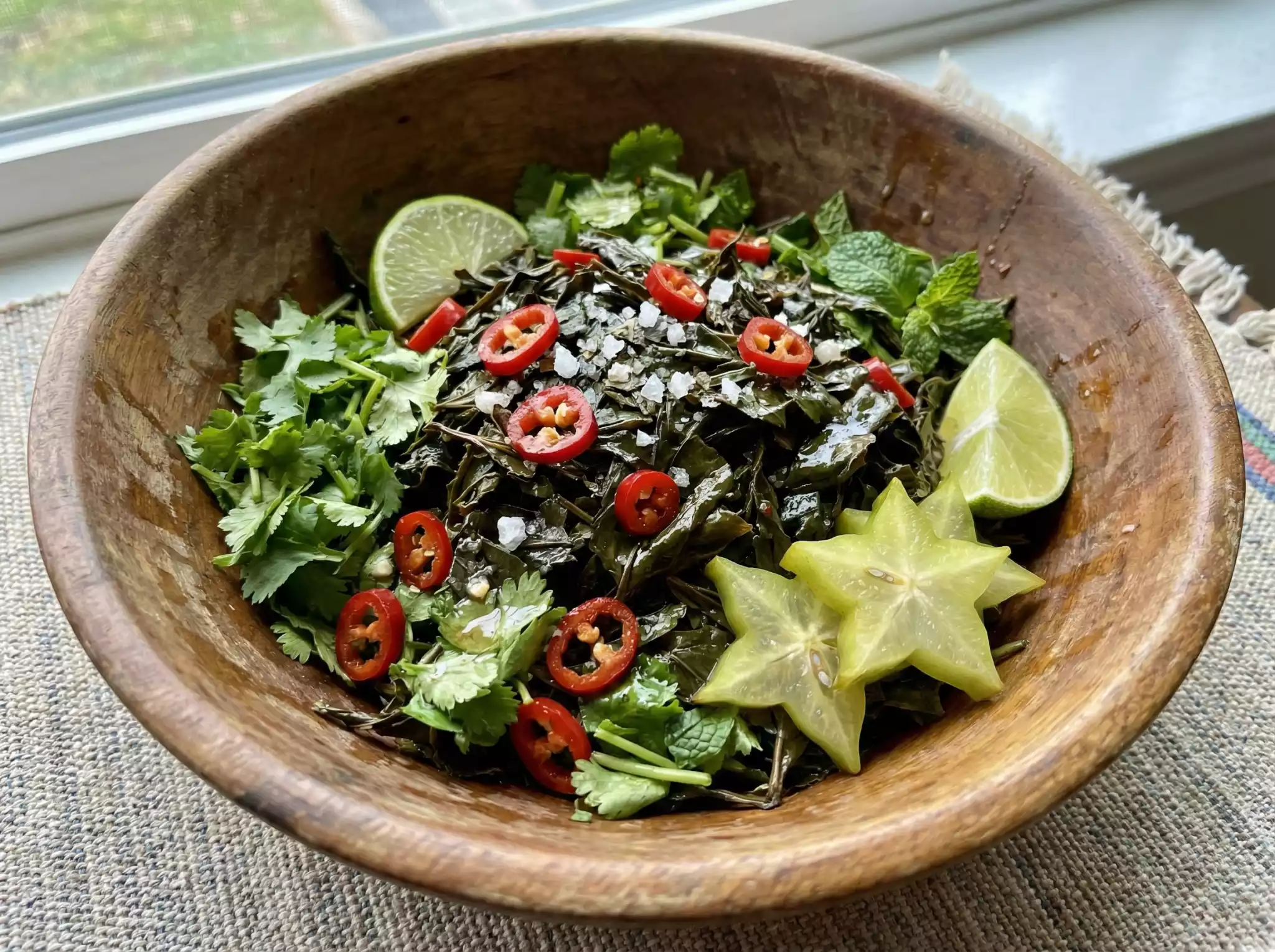 Bulang Liangban Cha: cold-mixed Pu-erh tea salad with fresh herbs, chili peppers, lime, and salt in a wooden bowl – traditional Yunnan delicacy
