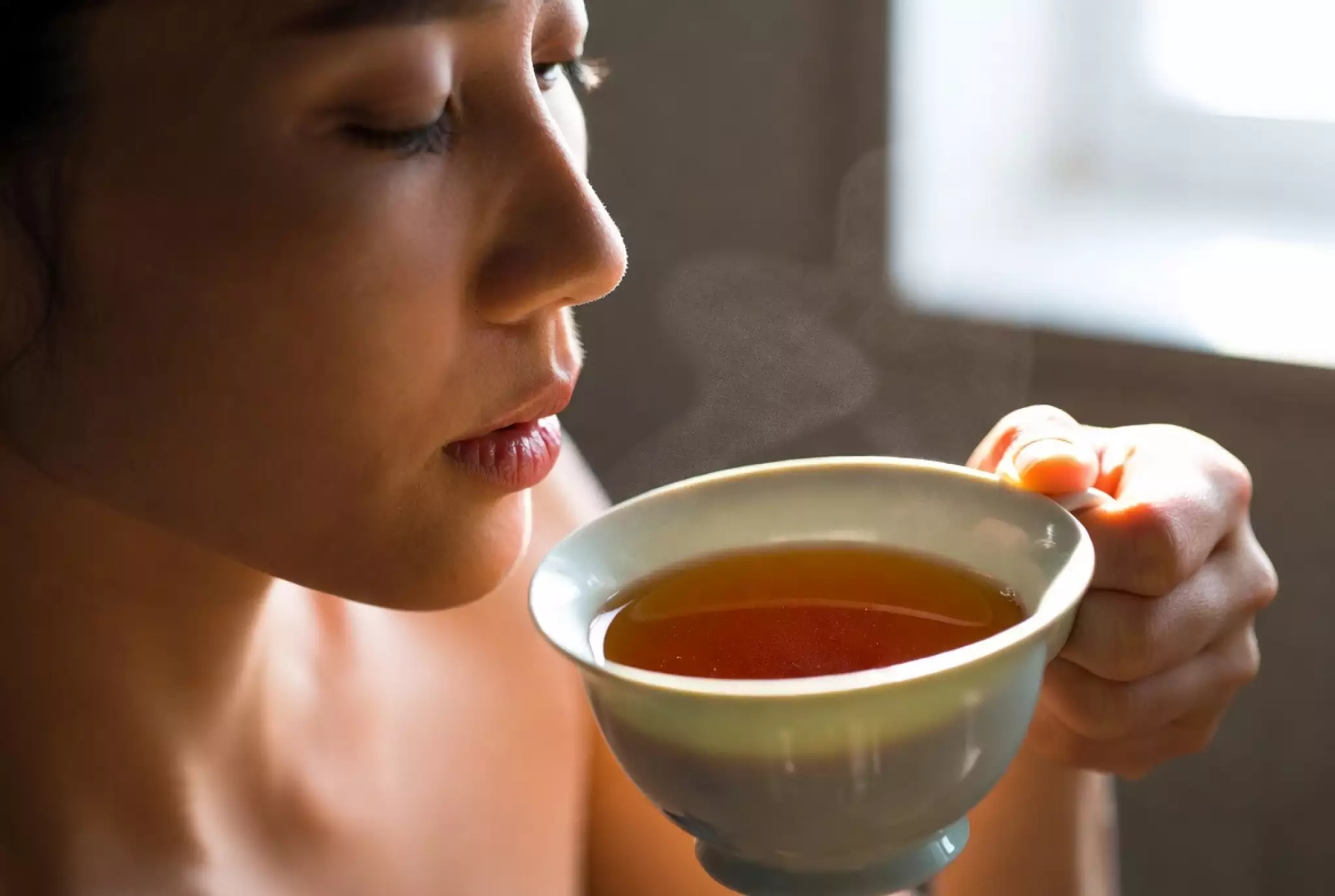Person gently inhaling the rich aroma rising from a warm white gaiwan filled with brewed tea