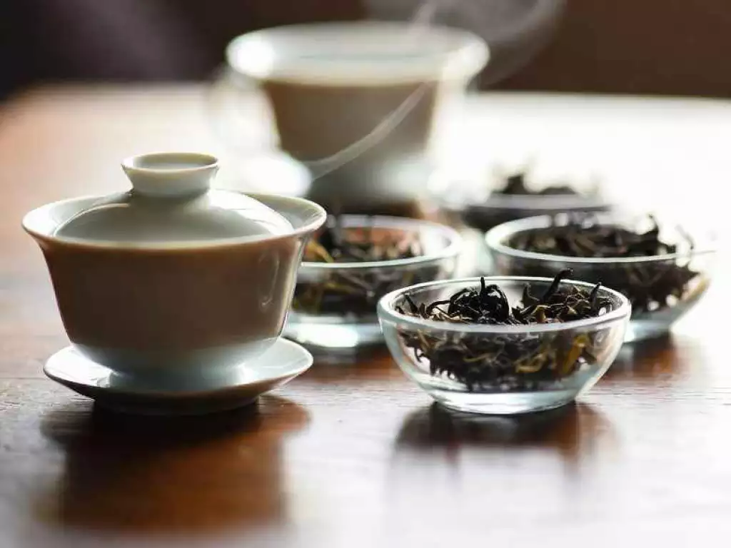 A serene tea-tasting setup with dry tea leaves in small bowls, a gaiwan, and a teapot, with gentle steam rising to evoke aroma
