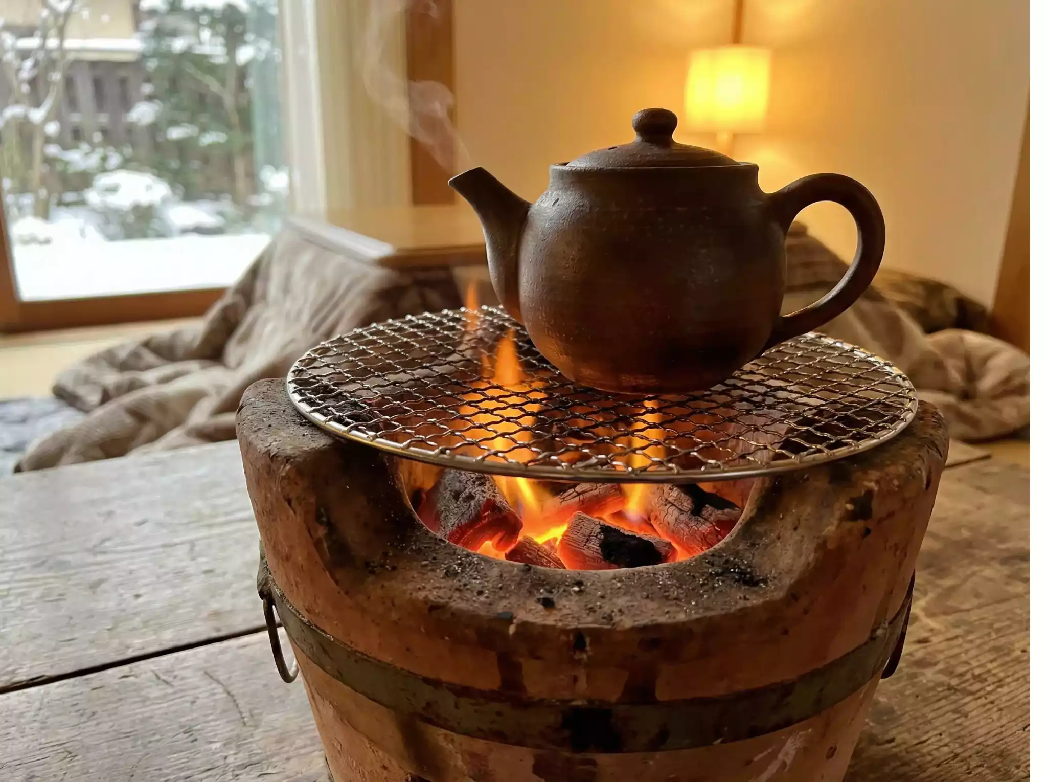 Close-up of traditional clay teapot simmering over glowing charcoal embers in a rustic indoor hearth, steam rising against snowy window backdrop