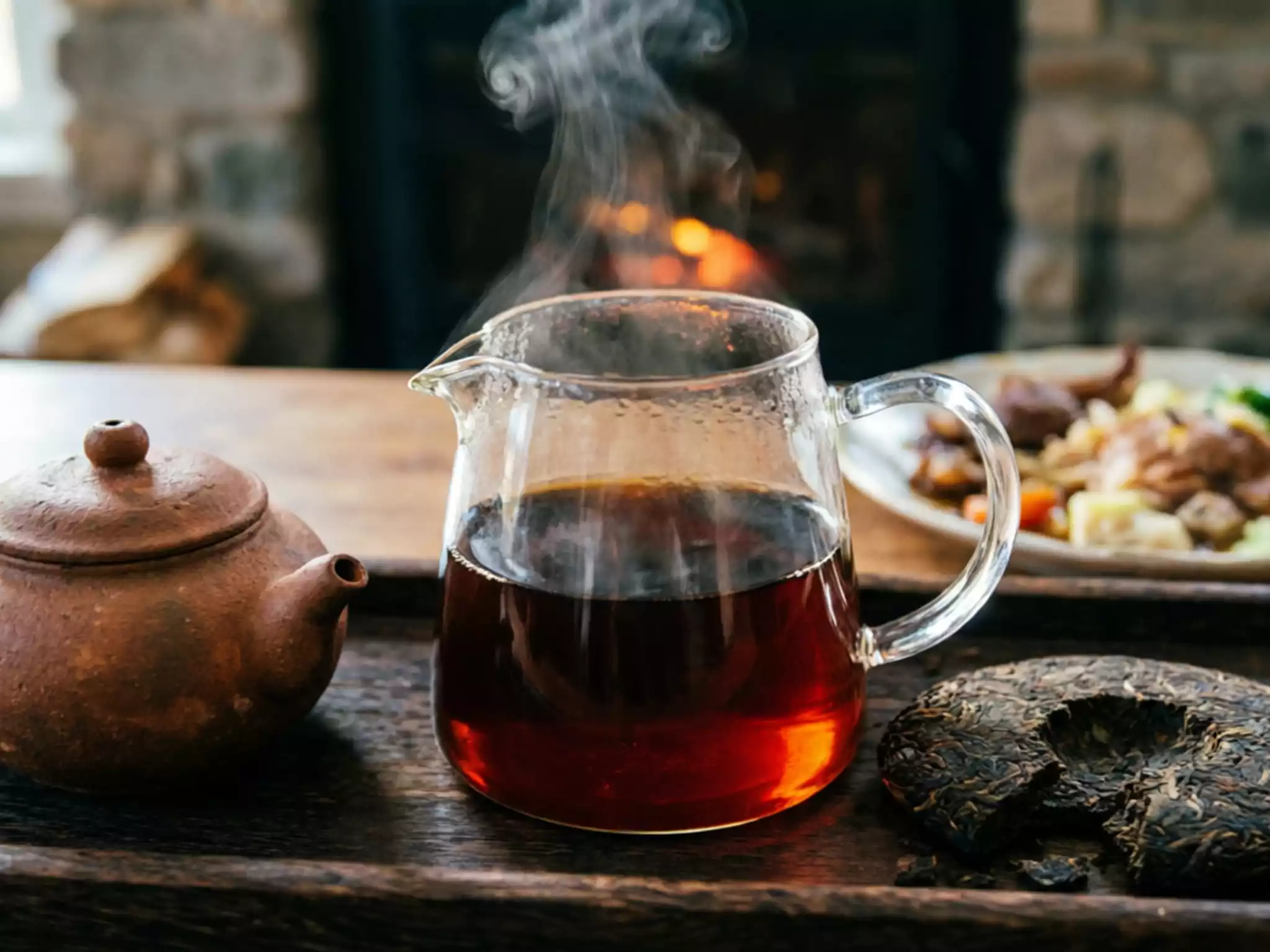 A close-up of dark reddish-brown Shou Pu-erh tea liquor in a glass pitcher with rising steam, symbolizing winter warmth