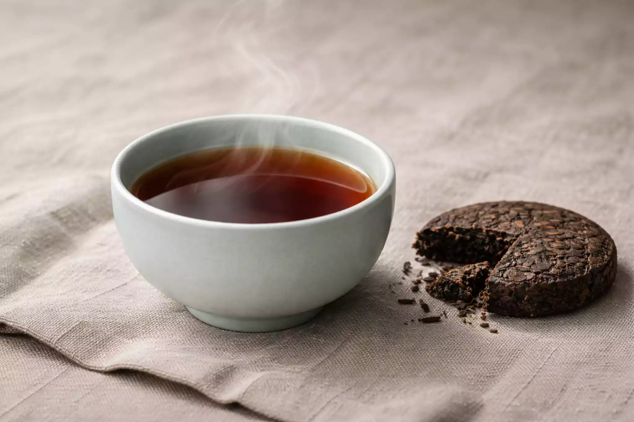 A traditional 357g Pu-erh tea cake alongside a modern glass server, showcasing the contrast between heritage and contemporary brewing.