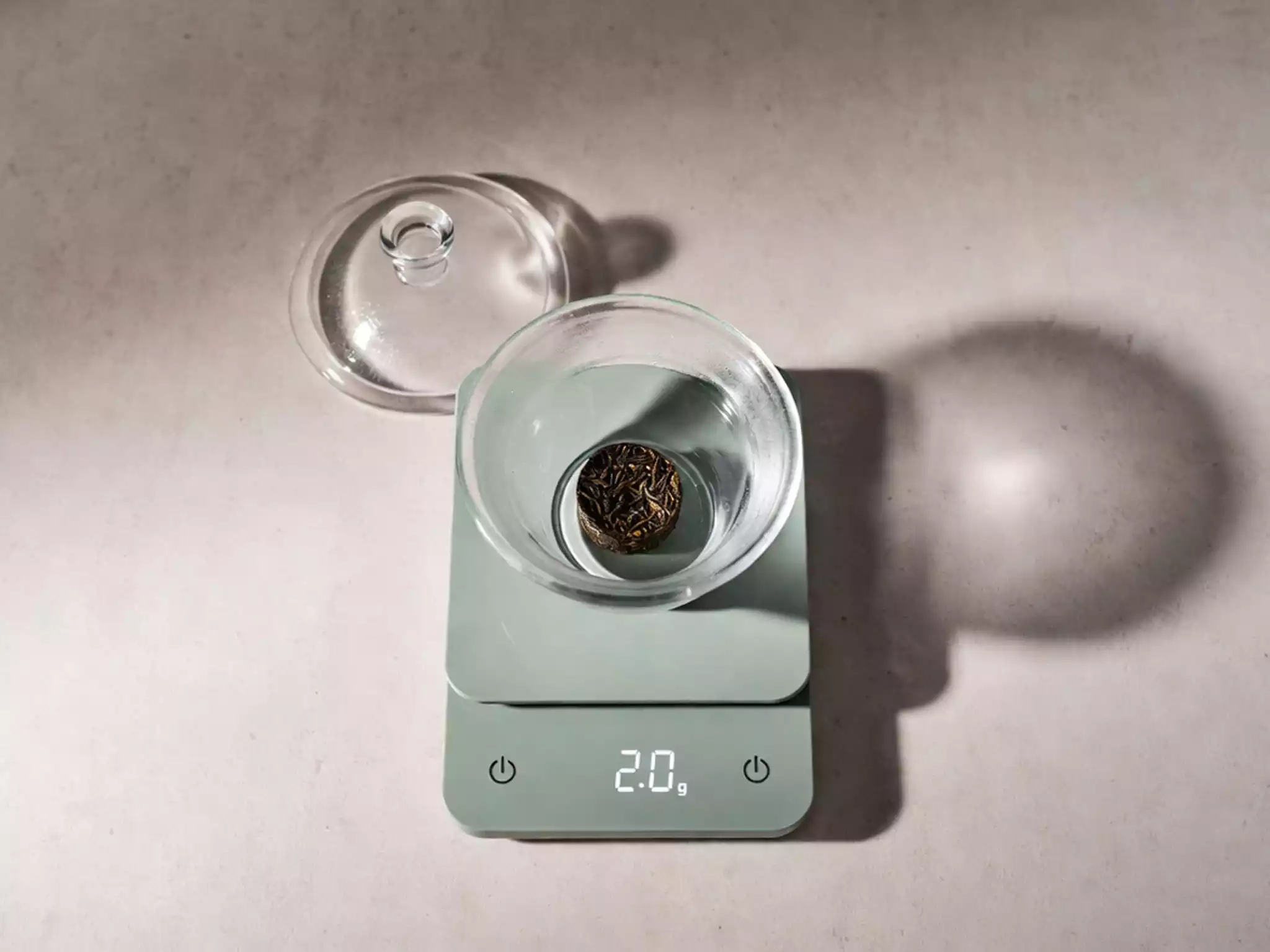 Minimalist tea brewing setup featuring a 2g tea coin cake on a digital scale for precision